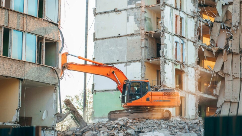 صورة توضح عملية هدم المباني، حيث يتم استخدام المعدات الثقيلة لتفكيك الهياكل الخرسانية
